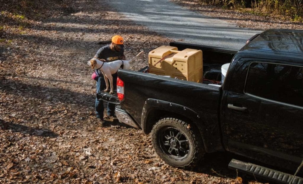 A hunter loads his pointer into a kennel in the bed of his truck.